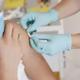 Ręce w niebieskich rękawiczkach zakładają plaster po szczepieniu 13 latka.