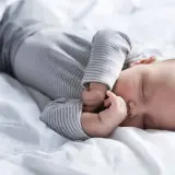 Słodki sen niemowlaka na białej pościeli. Tabela snu niemowlaka może pomóc zrozumieć jego potrzeby.