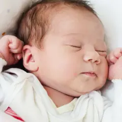 Śpiące 3-miesięczne dziecko, które przesypia 10 godzin w nocy bez jedzenia, wtulone w białą pościel w kolorowe kropki.