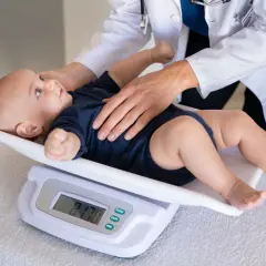 Lekarz waży niemowlę. Waga dziecka 3 miesiące to 8.170 kg.