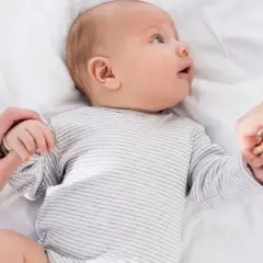 Niemowlę w paski, trzymające dłonie rodziców. U niemowlaka objawy wzmożone napięcie mięśniowe a sen.