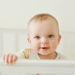 Uśmiechnięte dziecko w łóżeczku, jakby sprawdzało swój kalendarz rozwojowy.