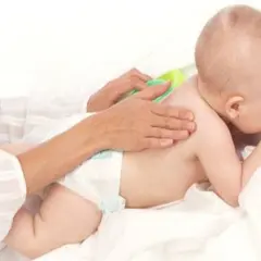 Delikatny masaż pleców dla dziecka, które waży 9 kg. Ręce opiekuna głaszczą maluszka.