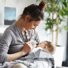 Kobieta karmi piersią dziecko, otulone kocykiem. Czy w ciąży można karmić piersią? To pytanie nurtuje wiele mam.