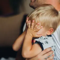 2-letnie dziecko budzi się w nocy z płaczem, ukrywając twarz w dłoniach. Tata tuli go, próbując uspokoić.
