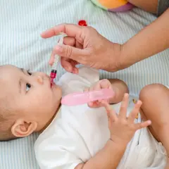 Podawanie witaminy D niemowlakowi rano czy wieczorem? Dłoń podaje dziecku syrop z witaminą D.