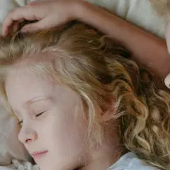 Dwie dziewczynki z blond włosami śpią blisko siebie. Jedna z nich ma rękę na głowie, co może sugerować niespokojny sen dwulatka.
