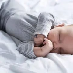 Słodki sen niemowlaka na białej pościeli. Tabela snu niemowlaka może pomóc zrozumieć jego potrzeby.