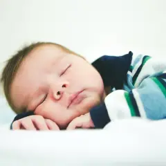 Słodki noworodek w pasiastej bluzce śpi spokojnie. Ile spi 5 tyg dziecko? Tyle, ile potrzebuje, by rosnąć!