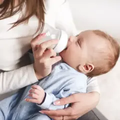 Ciepłe chwile karmienia mlekiem matki z butelki. Maluch pije, otoczony troską.