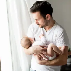 Ojciec tuli śpiące dziecko, które ma 24 tydzień życia. Delikatne światło wpada przez okno.