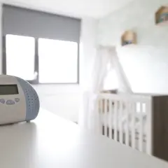 Niania elektroniczna czuwa, by usłyszeć każdy szumis dźwięk z pokoju dziecka. W tle białe łóżeczko i chmurki na ścianie.