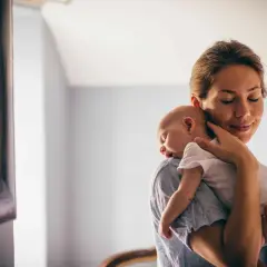 Delikatne odbijanie noworodka na ramieniu mamy. Spokojny sen maluszka, czuły dotyk matki.