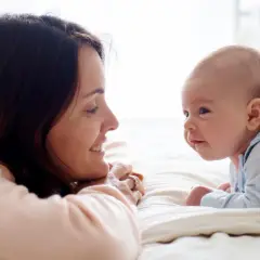 Uśmiechnięta mama patrzy na swojego 14-tygodniowego niemowlaka, który leży na brzuszku.