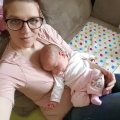 Mama z dzieckiem na rękach. Maluch śpi, jak widzi dziecko w 3 miesiącu, otoczony troską.