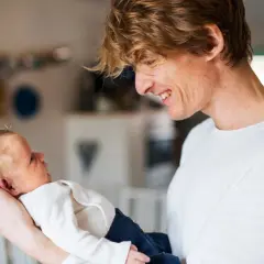 Uśmiechnięty tata trzyma na rękach swoje **12 tygodniowe dziecko**.