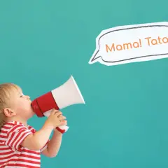 Mały chłopiec w czerwono-białej koszulce trzyma megafon, z którego wydobywa się "Mama! Tata!". To uroczy moment, kiedy dziecko zaczyna gaworzyć.