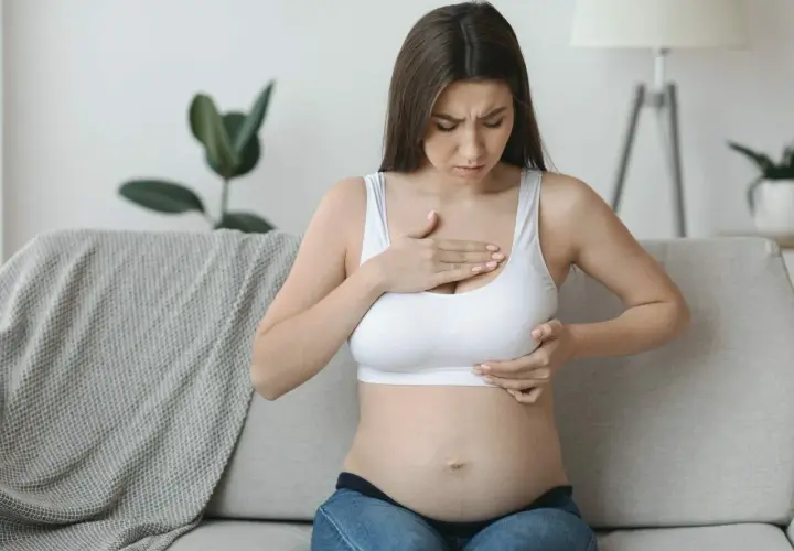 Kobieta w ciąży dotyka piersi, odczuwając dyskomfort. Jej twarz wyraża zaniepokojenie.