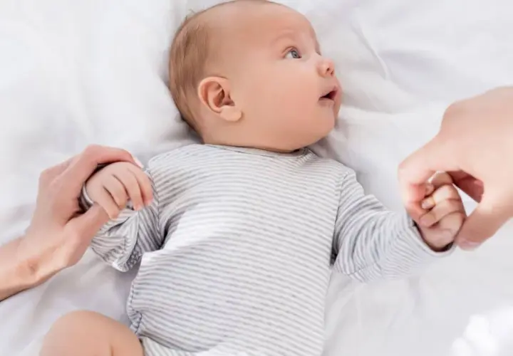 Niemowlę w paski, trzymające dłonie rodziców. U niemowlaka objawy wzmożone napięcie mięśniowe a sen.