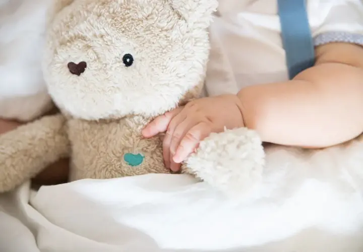 Niemowlę tuli pluszowego misia, przygotowując się do turbo drzemki. Miękkie futerko i delikatna rączka tworzą obraz spokoju.