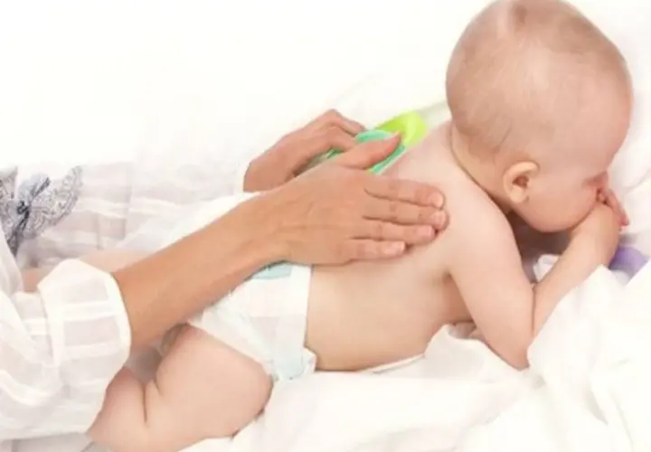 Delikatny masaż pleców dla dziecka, które waży 9 kg. Ręce opiekuna głaszczą maluszka.