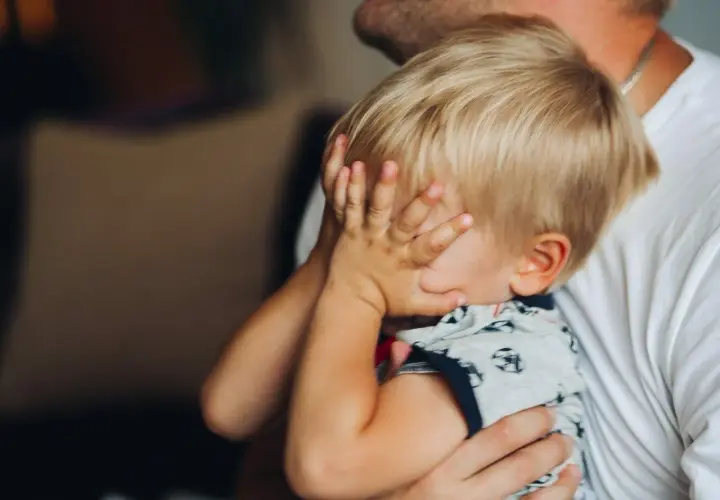 2-letnie dziecko budzi się w nocy z płaczem, ukrywając twarz w dłoniach. Tata tuli go, próbując uspokoić.