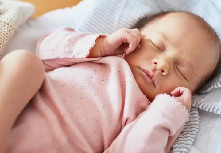 Słodko śpiące niemowlę w różowym ubranku. Zastanawiasz się, ile powinno spać roczne dziecko? Ten maluch odpoczywa, zbierając siły na kolejne przygody.
