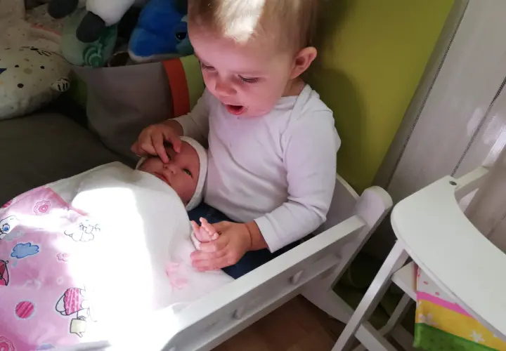 Starszy brat opiekuje się młodszym, który leży w łóżeczku. To piękny przykład skoku rozwojowego 18 miesiąc, gdy dzieci uczą się empatii.