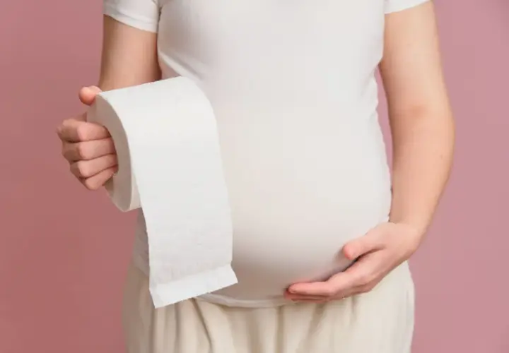 Kobieta w ciąży trzyma rolkę papieru toaletowego, sugerując problem z biegunką w ciąży.
