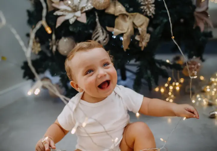 Uśmiechnięte dziecko z niebieskimi oczami bawi się lampkami choinkowymi. To magiczny moment, kiedy dziecko zaczyna mówić, pełen radości i odkryć.