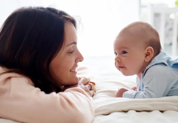 Uśmiechnięta mama patrzy na swojego 14-tygodniowego niemowlaka, który leży na brzuszku.