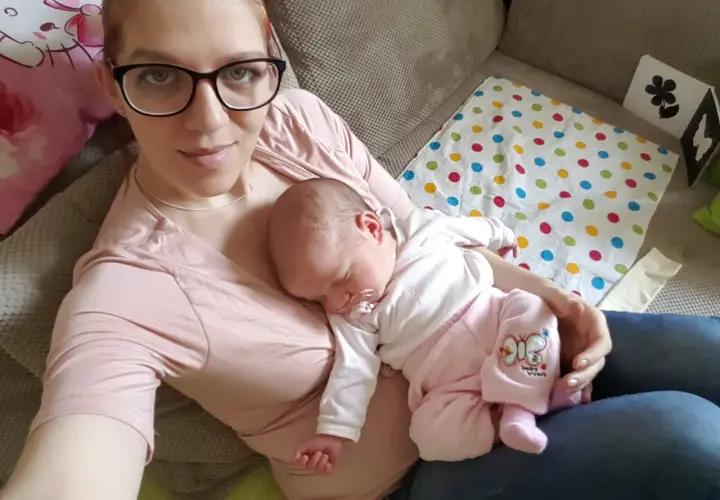 Mama z dzieckiem na rękach. Maluch śpi, jak widzi dziecko w 3 miesiącu, otoczony troską.