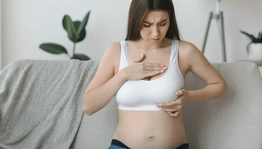 Kobieta w ciąży dotyka piersi, odczuwając dyskomfort. Jej twarz wyraża zaniepokojenie.