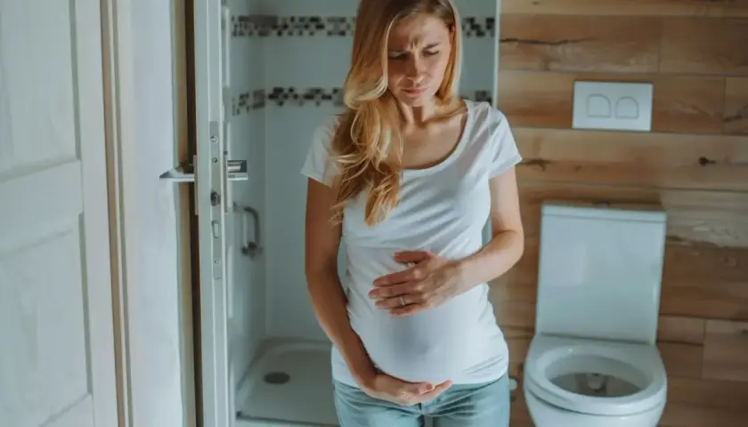 Kobieta w ciąży, w 3 trymestrze, trzyma się za brzuch z powodu bólu brzucha jak na okres.