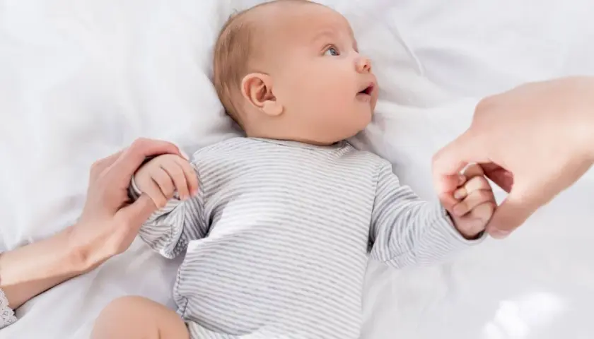 Niemowlę w paski, trzymające dłonie rodziców. U niemowlaka objawy wzmożone napięcie mięśniowe a sen.