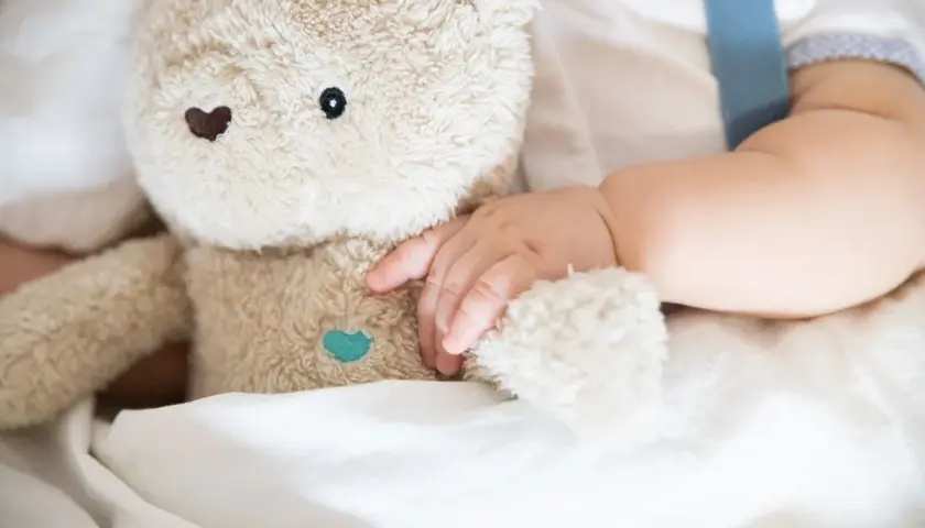 Niemowlę tuli pluszowego misia, przygotowując się do turbo drzemki. Miękkie futerko i delikatna rączka tworzą obraz spokoju.