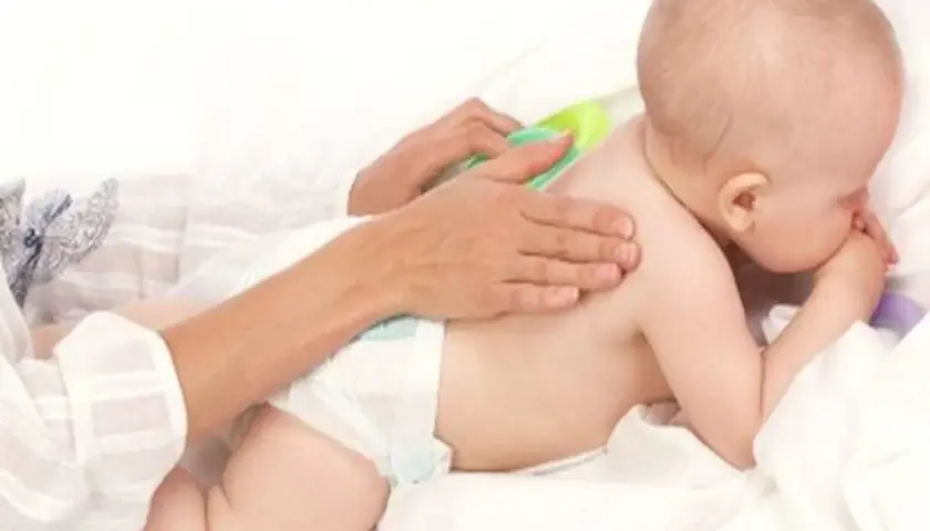 Delikatny masaż pleców dla dziecka, które waży 9 kg. Ręce opiekuna głaszczą maluszka.