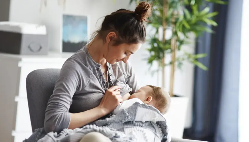 Kobieta karmi piersią dziecko, otulone kocykiem. Czy w ciąży można karmić piersią? To pytanie nurtuje wiele mam.