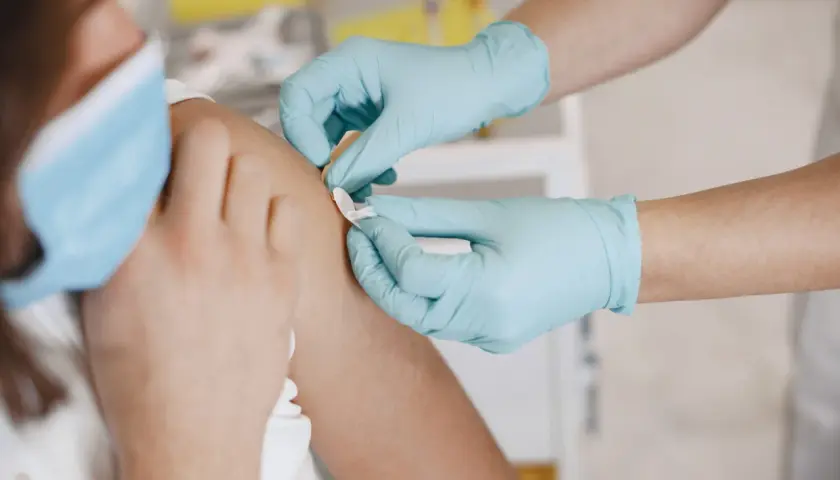Ręce w niebieskich rękawiczkach zakładają plaster po szczepieniu 13 latka.