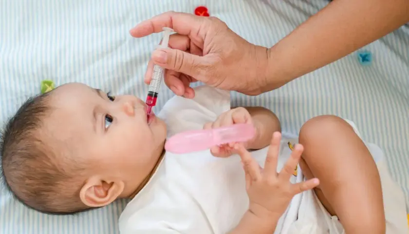 Podawanie witaminy D niemowlakowi rano czy wieczorem? Dłoń podaje dziecku syrop z witaminą D.