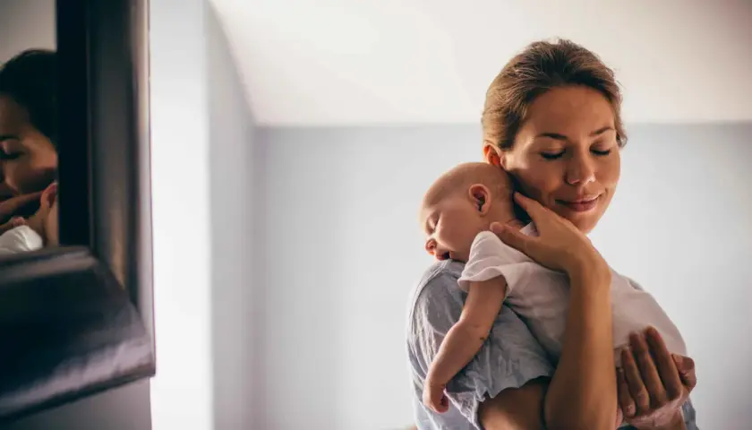 Delikatne odbijanie noworodka na ramieniu mamy. Spokojny sen maluszka, czuły dotyk matki.