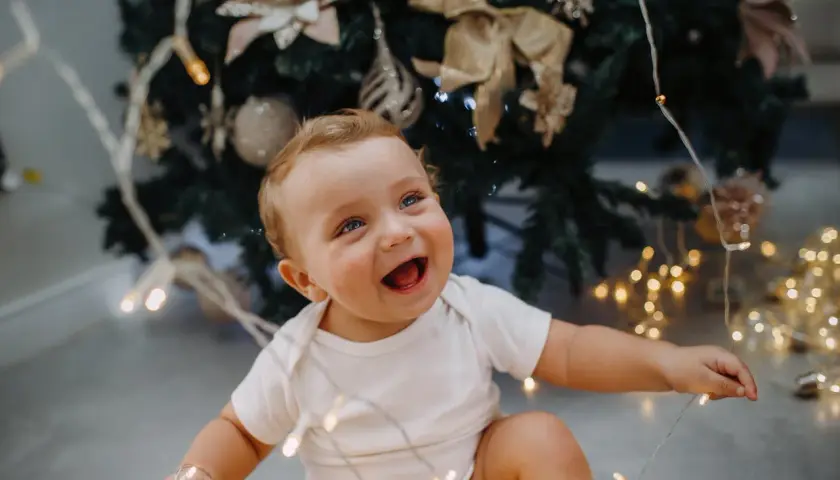 Uśmiechnięte dziecko z niebieskimi oczami bawi się lampkami choinkowymi. To magiczny moment, kiedy dziecko zaczyna mówić, pełen radości i odkryć.