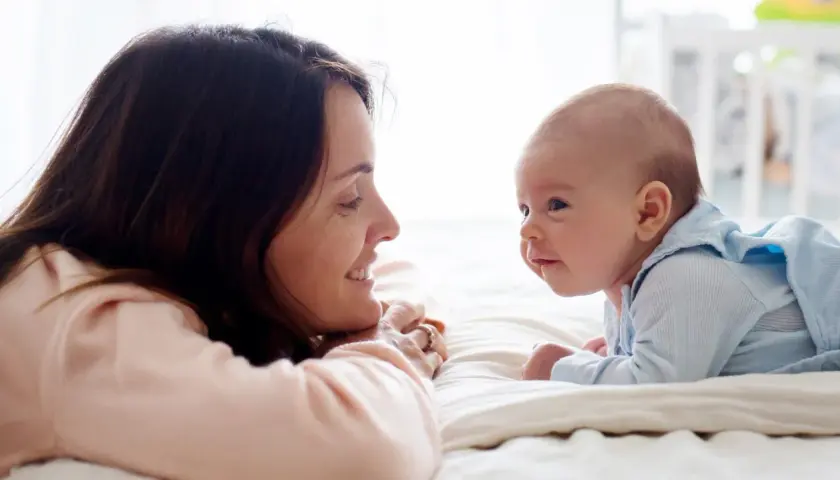 Uśmiechnięta mama patrzy na swojego 14-tygodniowego niemowlaka, który leży na brzuszku.