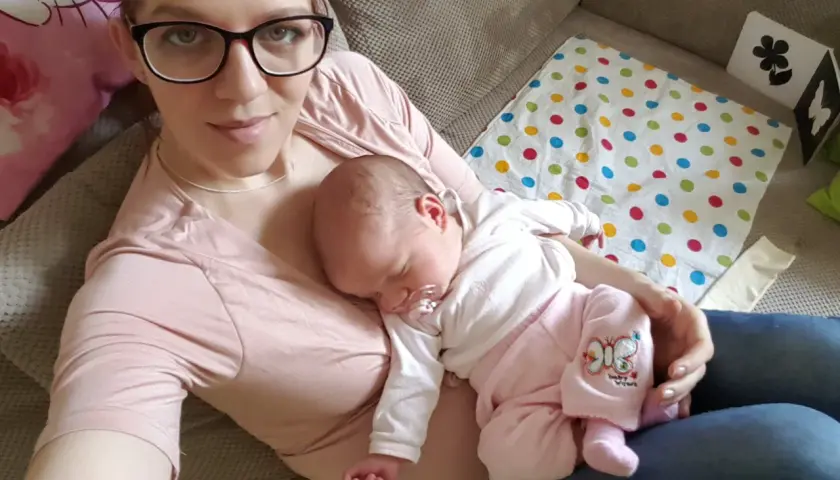 Mama z dzieckiem na rękach. Maluch śpi, jak widzi dziecko w 3 miesiącu, otoczony troską.