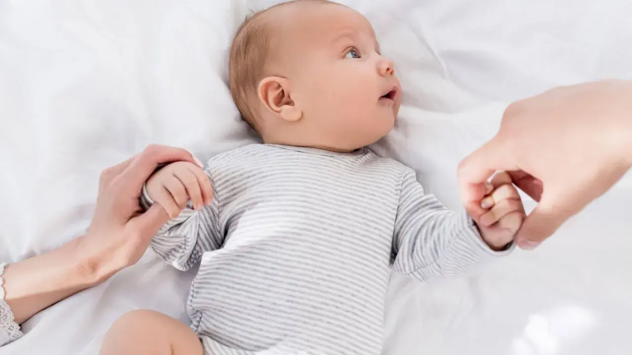 Niemowlę w paski, trzymające dłonie rodziców. U niemowlaka objawy wzmożone napięcie mięśniowe a sen.