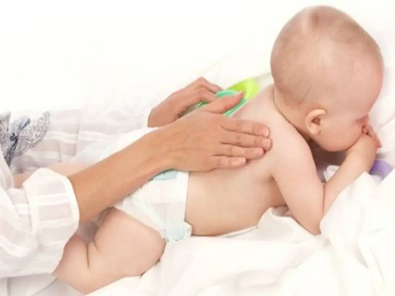 Delikatny masaż pleców dla dziecka, które waży 9 kg. Ręce opiekuna głaszczą maluszka.