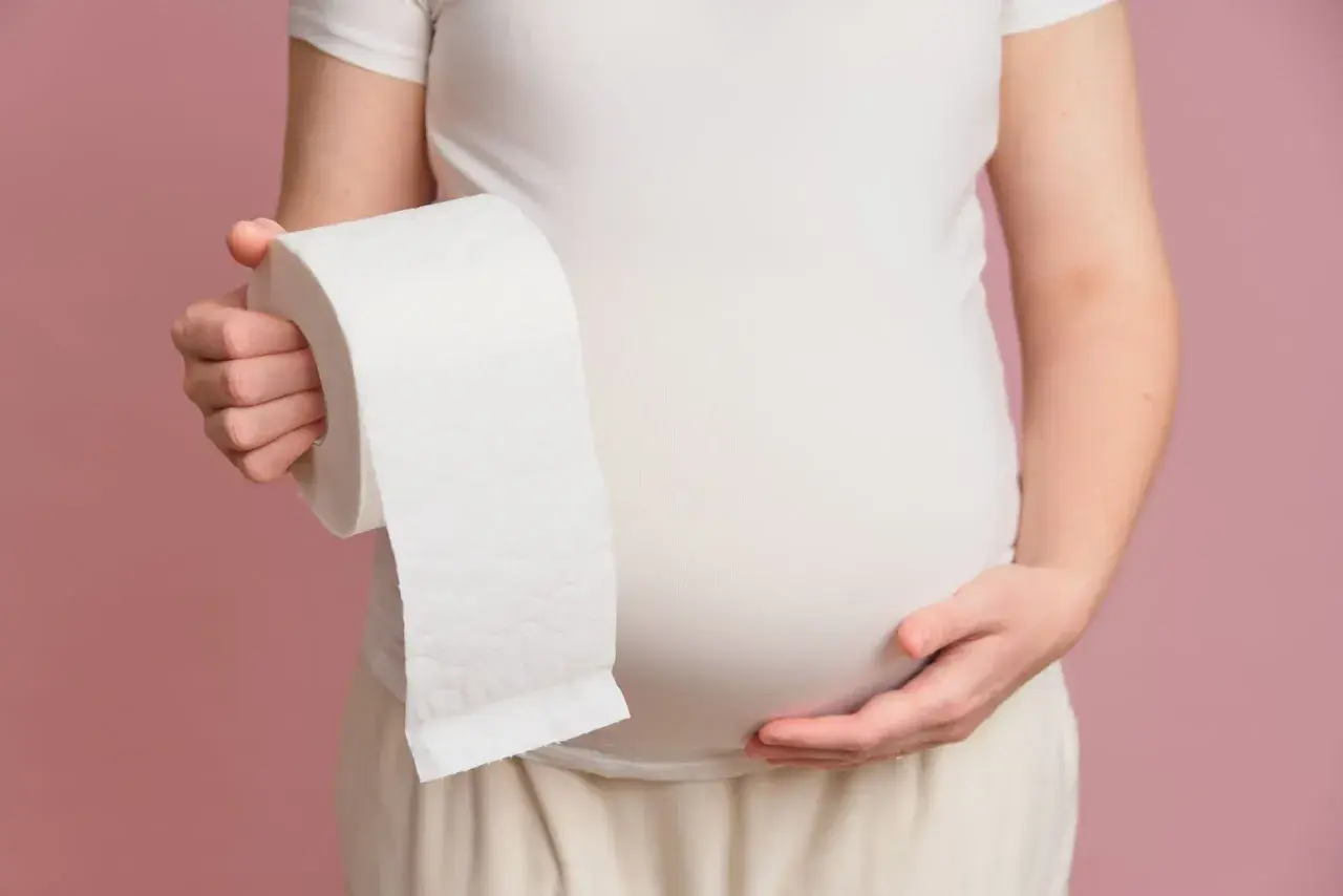 Kobieta w ciąży trzyma rolkę papieru toaletowego, sugerując problem z biegunką w ciąży.