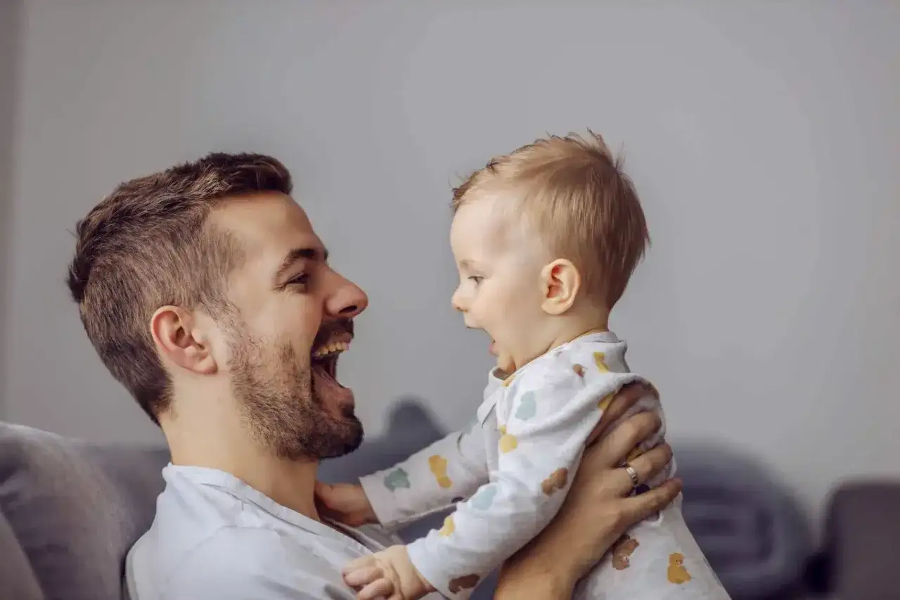 Ojciec śmieje się radośnie, gdy jego dziecko zaczyna głużyć, patrząc mu w oczy.