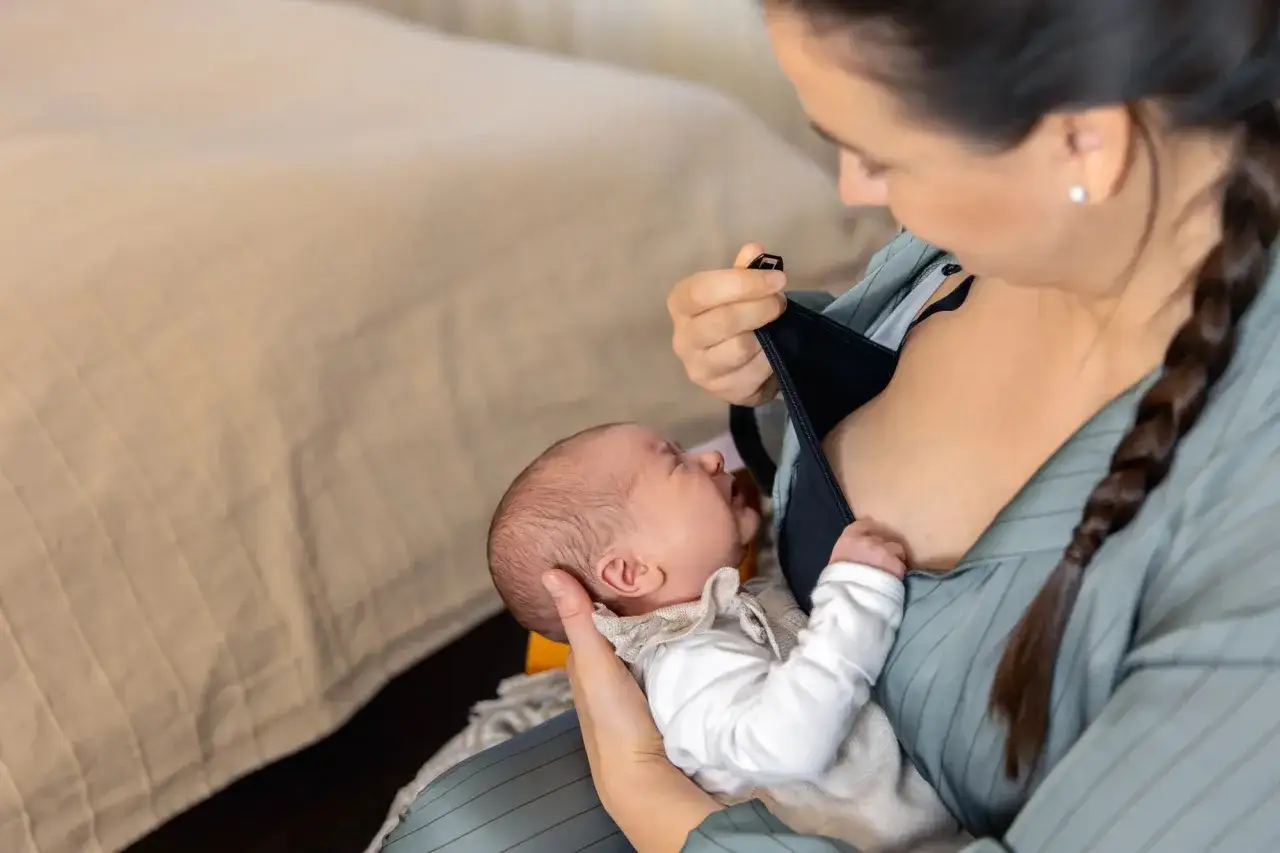 Mama karmi piersią noworodka, wspierając naturalne karmienie i pokazując, jak pobudzić laktację.