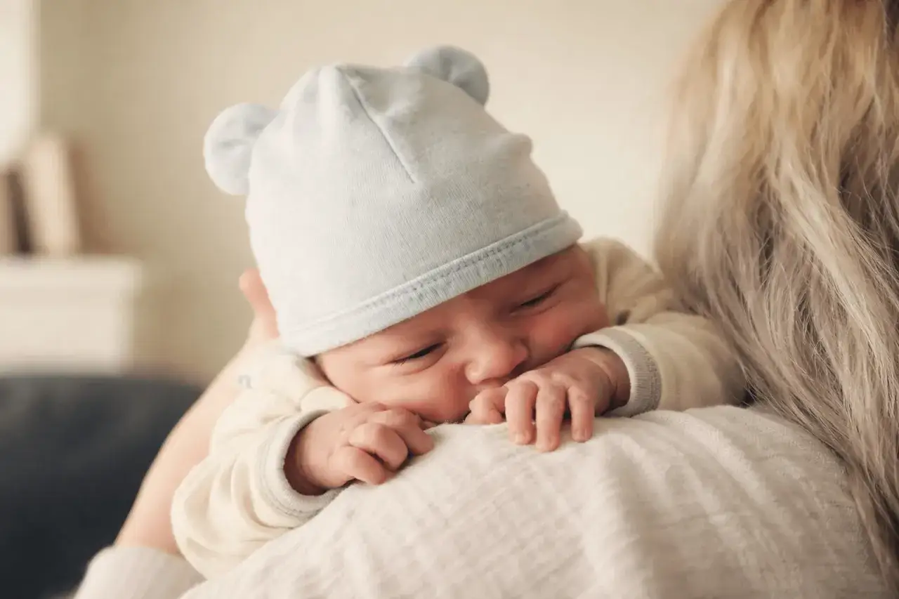 Malutkie dziecko w niebieskiej czapeczce z uszkami wtulone w ramię mamy. Czas, kiedy dziecko przestaje mieć drzemki, jest pełen czułości.